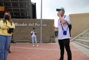 Joven guía de Bogotá Colors habla a invitados a recorrido, al fondo, estación de transmicabler