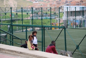 Al fondo cancha de fútbol y niño sonríe a la cámara